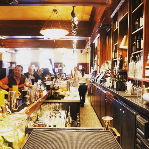 A bustling bar scene with patrons, bartenders, and shelves of liquor in a warm, inviting atmosphere.