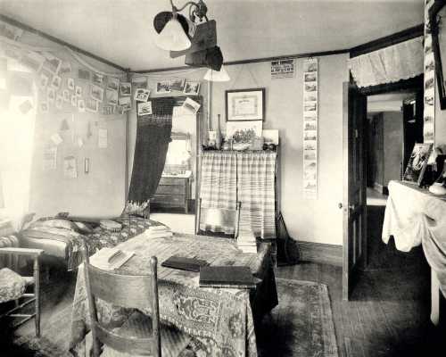 A vintage room with a bed, table, and chairs, decorated with photos and postcards on the walls.