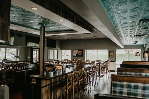 Interior of a restaurant featuring wooden bar, high chairs, and a decorative ceiling, with large windows and booths.
