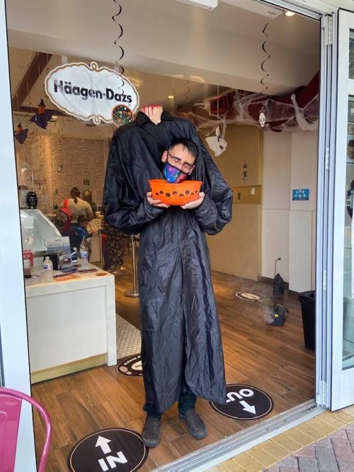 A person in a black cloak holds a bowl while standing in front of a Häagen-Dazs store decorated for Halloween.