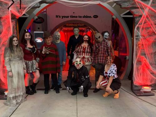A group of people in Halloween costumes, posing in a spooky setting with red lighting and decorations.