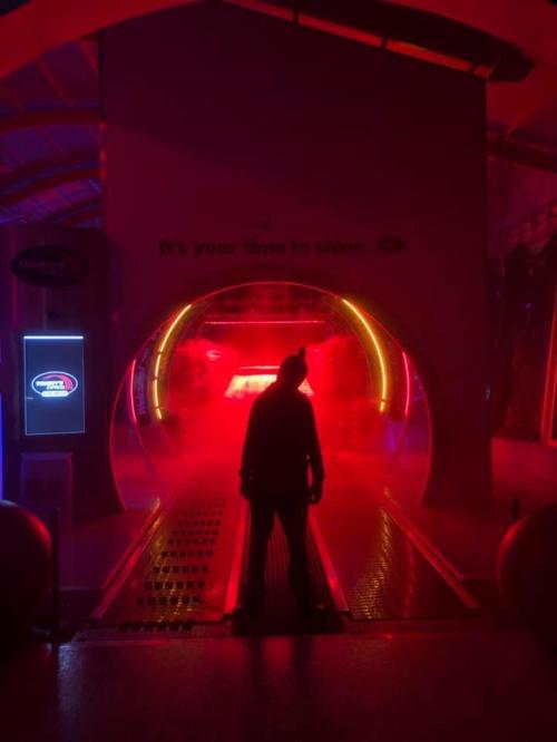 A silhouetted figure stands in a brightly lit, misty tunnel with colorful lights, creating a dramatic atmosphere.