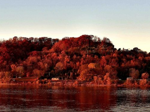 Autumn landscape with vibrant red and orange foliage reflecting on calm water at sunset.
