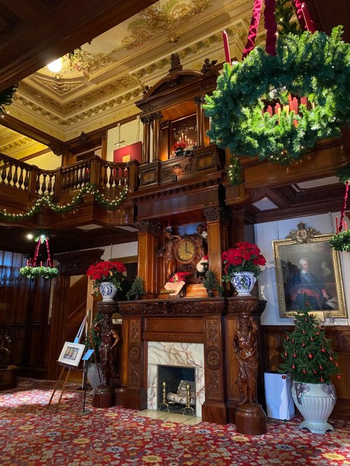 A beautifully decorated room with a wooden fireplace, festive wreaths, and holiday decorations throughout.