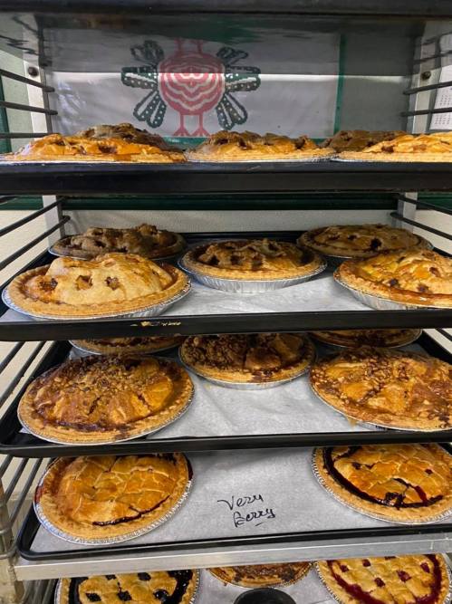 A display of various pies on shelves, including apple, pecan, and berry, in a bakery setting.