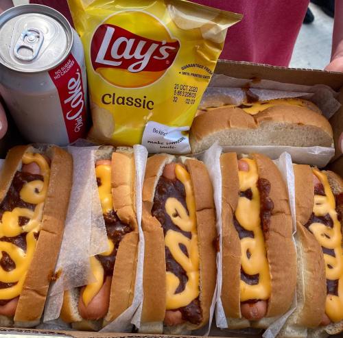 A tray of hot dogs topped with cheese and chili, alongside a bag of Lay's chips and a soda can.