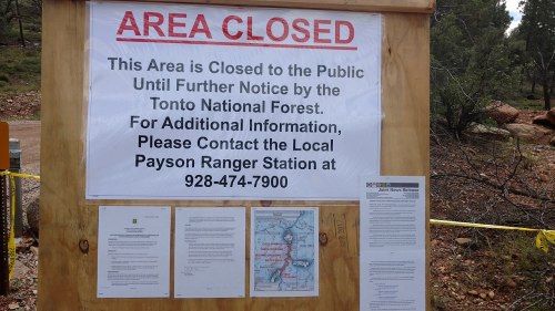 Sign on a wooden board stating "Area Closed" with contact information for the Payson Ranger Station and a map.