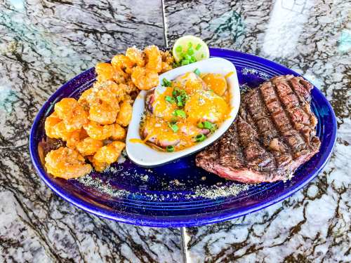 A vibrant plate featuring grilled steak, shrimp in sauce, and crispy fried shrimp, garnished with lime and green onions.