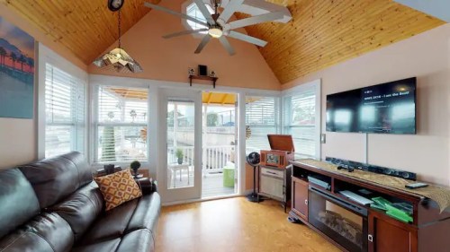 Cozy living room with a ceiling fan, large windows, and a TV, featuring a leather sofa and access to a deck.