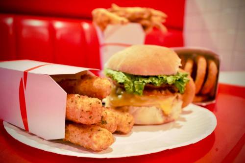 A plate with a burger topped with lettuce and cheese, alongside a box of crispy mozzarella sticks and fries.
