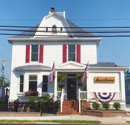 A charming white house with red shutters, American flags, and a welcoming porch, set against a clear blue sky.
