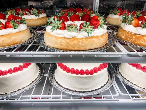 A display of three cakes in a refrigerator, topped with strawberries and raspberries, with whipped cream decorations.