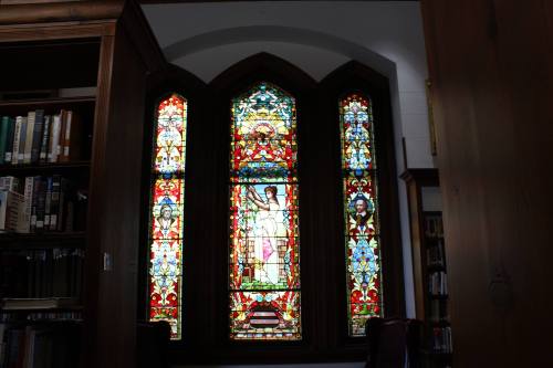 Stained glass window featuring colorful biblical figures and intricate designs, set in a library.