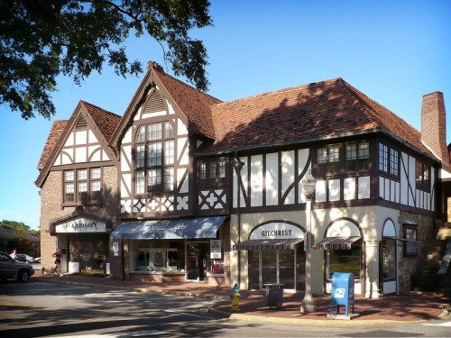 A charming Tudor-style building with shops and a blue mailbox in a sunny urban setting.