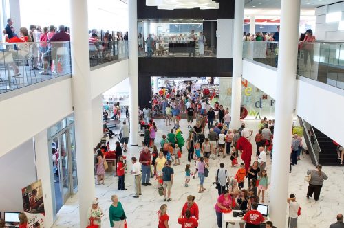 A busy shopping mall filled with crowds of people on multiple levels, with bright lighting and modern architecture.