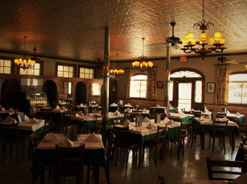 A cozy restaurant interior with wooden tables, chairs, and vintage decor, featuring warm lighting and a welcoming atmosphere.