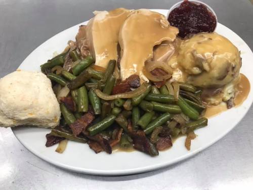 A plate of turkey with gravy, green beans, mashed potatoes, a biscuit, and a side of cranberry sauce.