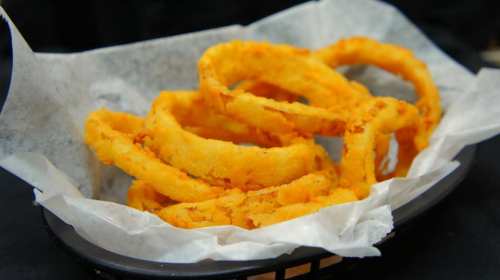 A basket of crispy, golden-brown onion rings on parchment paper.