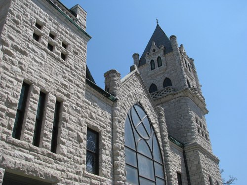 A tall stone building with a pointed tower and large arched windows against a clear blue sky.