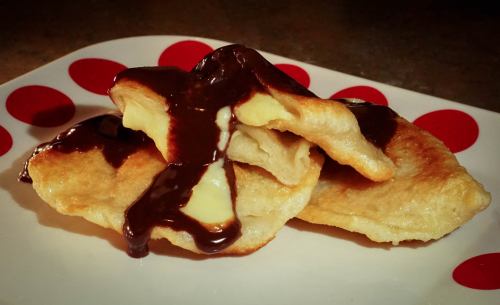 Three golden-brown dumplings drizzled with rich chocolate sauce on a red polka dot plate.