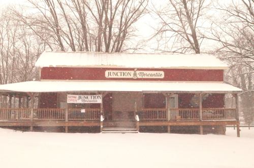 A red mercantile building covered in snow, with a sign reading "Junction Mercantile" and a snowy landscape.