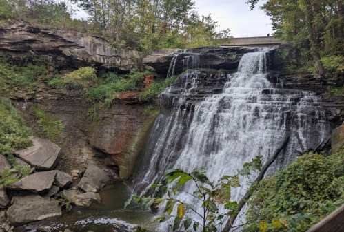 A scenic waterfall cascading over rocky cliffs, surrounded by lush greenery and trees.