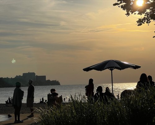 Silhouettes of people at a beach during sunset, with an umbrella and calm water in the background.