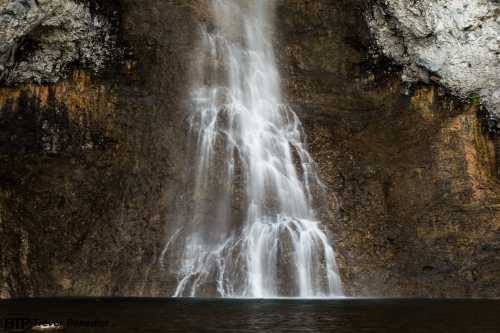 A cascading waterfall flows down a rocky cliff into a serene pool below, surrounded by textured stone walls.