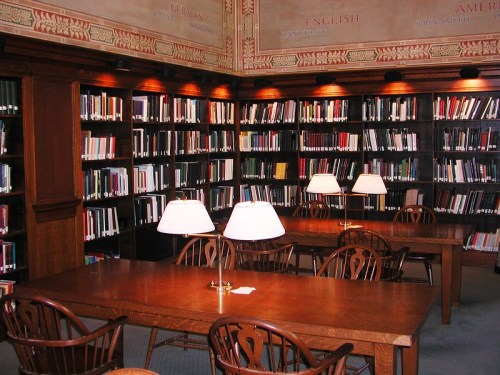 A cozy library with wooden tables, lamps, and shelves filled with books in a warm, inviting atmosphere.