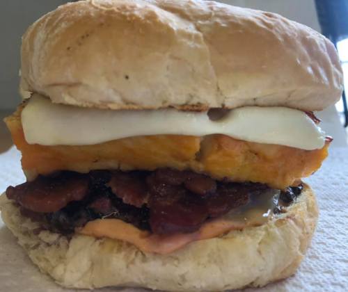 A close-up of a sandwich with layers of bacon, cheese, and a golden-brown biscuit bun.