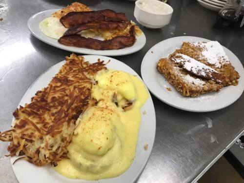 A plate of eggs Benedict with hash browns, crispy bacon, and a side of powdered sugar-dusted French toast.