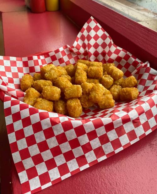 A basket of golden, crispy tater tots on a red and white checkered paper.