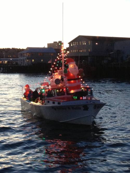 A decorated boat with festive lights and inflatable Santa, sailing on water at dusk.