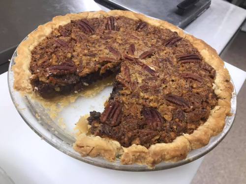 A pecan pie with a slice removed, showcasing a golden crust and a rich, nutty filling topped with whole pecans.