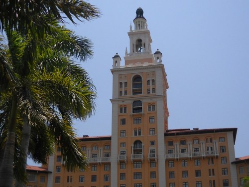 Historic building with a tall clock tower, surrounded by palm trees against a clear blue sky.