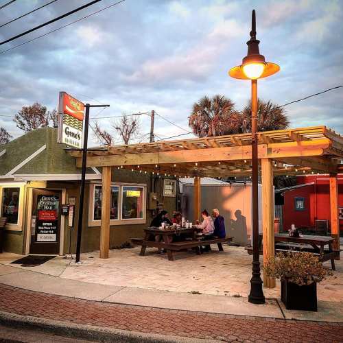 Outdoor dining area of a restaurant with a wooden pergola, tables, and a cozy evening atmosphere.