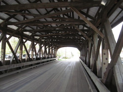 Interior view of a wooden covered bridge, showcasing its structural beams and a pathway leading to the exit.