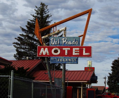 Vintage Del Prado Motel sign with "Vacancy" displayed, set against a cloudy sky and surrounded by trees.