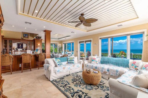 Bright, airy living room with coastal decor, large windows, and ocean views, featuring comfortable seating and a bar area.