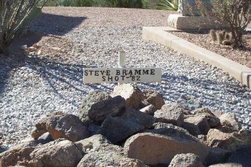 A weathered sign reading "Steve Bramme Shot '82" placed among rocks in a gravel area.