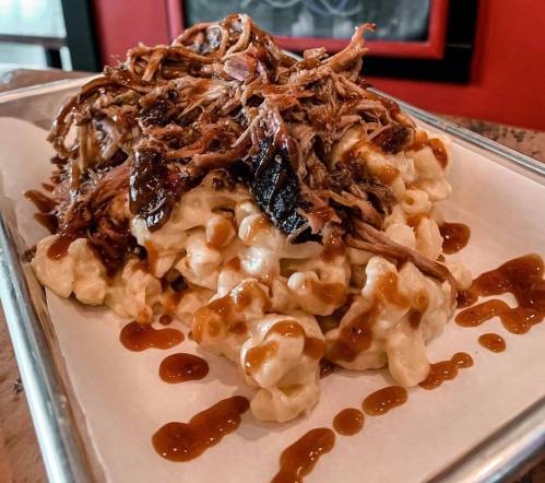 A plate of creamy macaroni and cheese topped with pulled pork and drizzled with barbecue sauce.