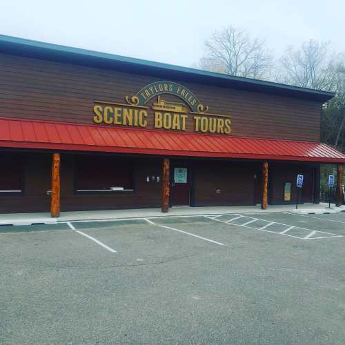 A wooden building with a sign reading "Scenic Boat Tours" and a parking lot in front, under a cloudy sky.