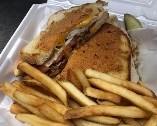 A grilled sandwich with layers of meat and cheese, served with a side of golden French fries and a pickle.