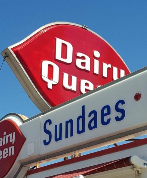 Sign for Dairy Queen featuring the word "Sundaes" against a clear blue sky.
