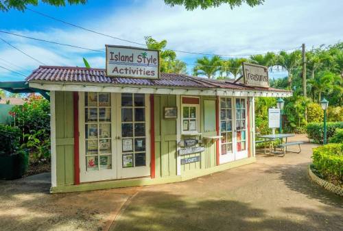 A colorful kiosk with signs for "Island Style Activities" and "Treasures," surrounded by lush greenery.