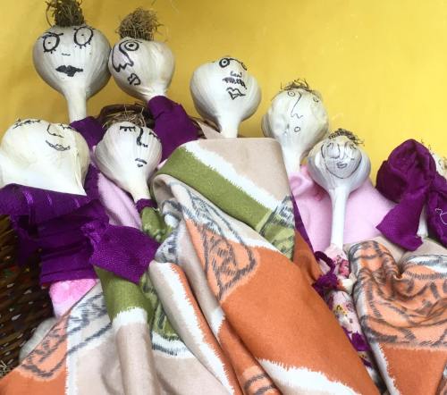 A group of decorated wooden spoons with faces, wrapped in colorful fabric, against a yellow background.