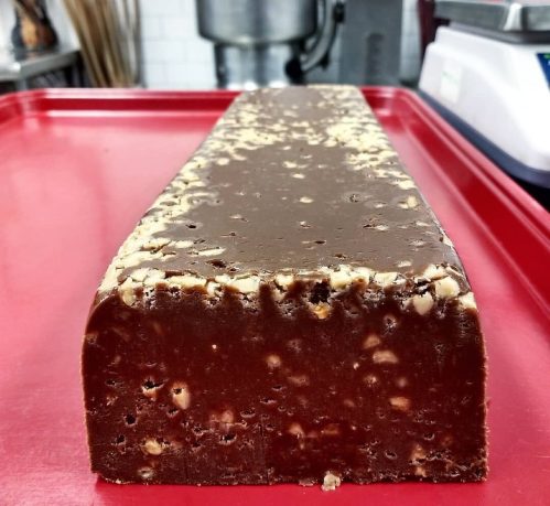 A large block of chocolate fudge with nuts, resting on a red tray in a kitchen setting.