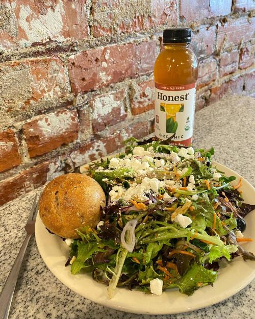 A fresh salad with mixed greens, feta cheese, and a whole grain roll, accompanied by a bottle of Honest tea.