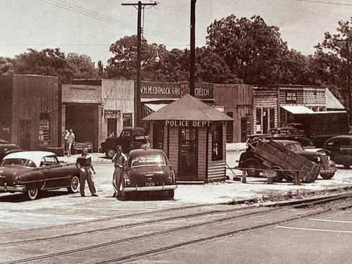 Black and white photo of a small town with vintage cars and a police department building.
