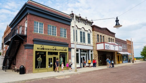A street view of historic buildings with shops and a theater, featuring people walking along the sidewalk.